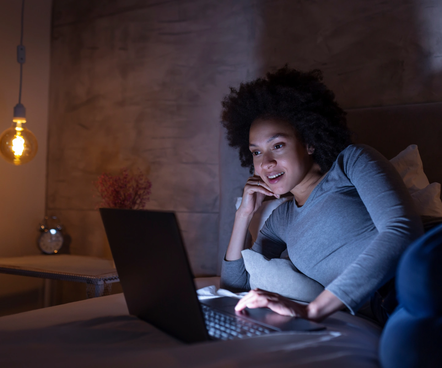A woman laying in bed with dim light using her laptop with Frontier internet
