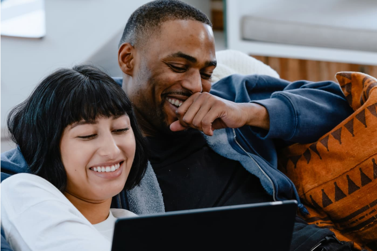 Man in a blue hoodie and woman in a white sweater watching YouTube TV on a laptop.