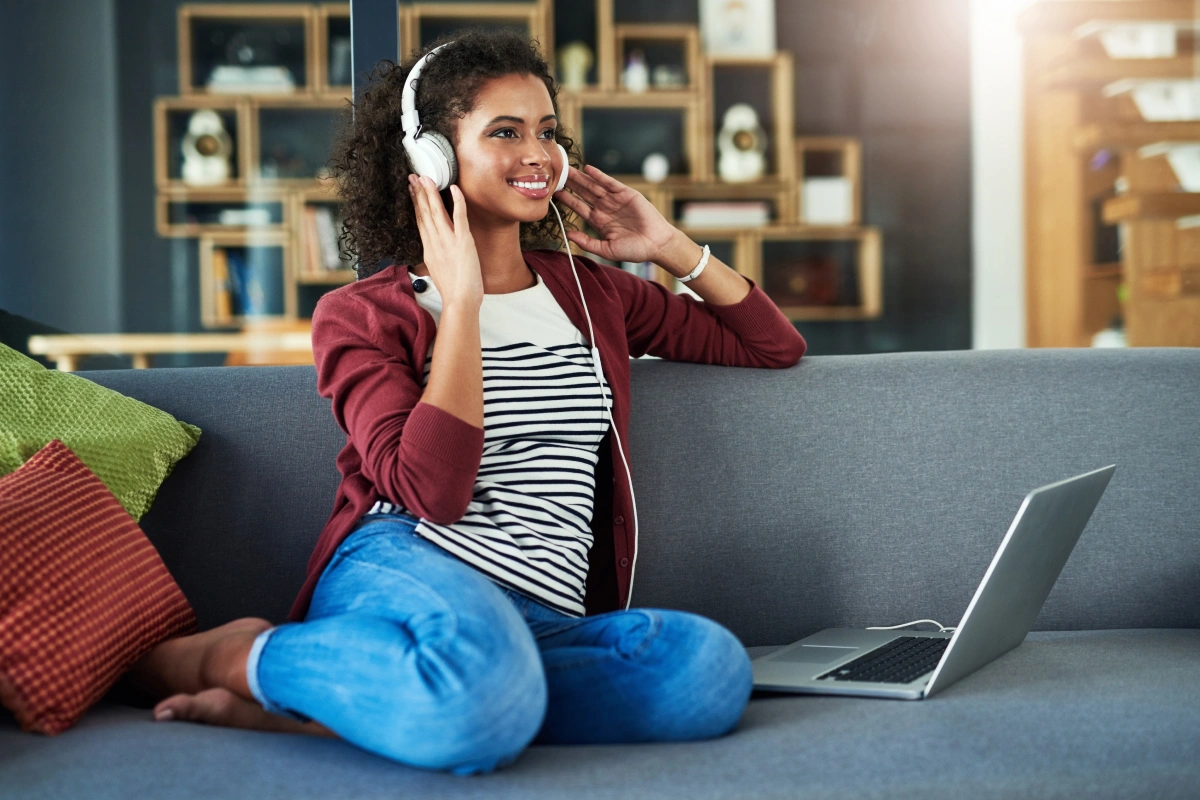A young woman sitting on her couch listening to TV with headphones on