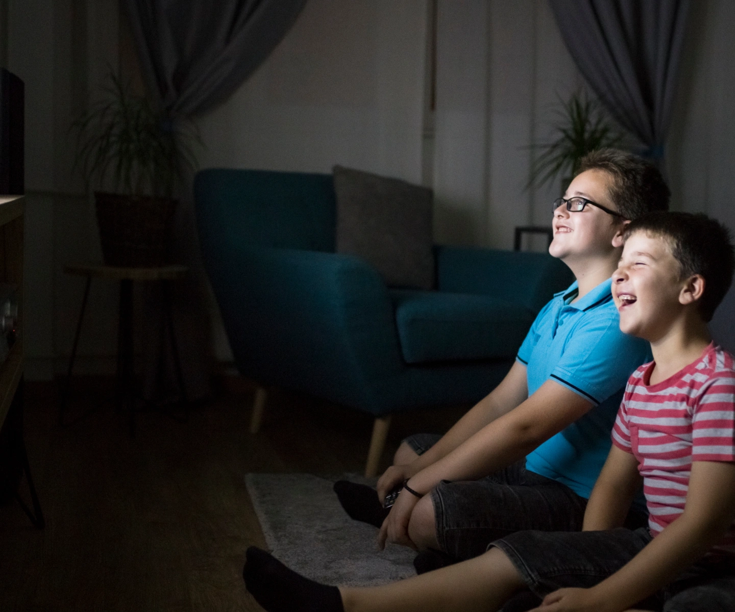 Two boys smiling and laughing as they sit and watch TV