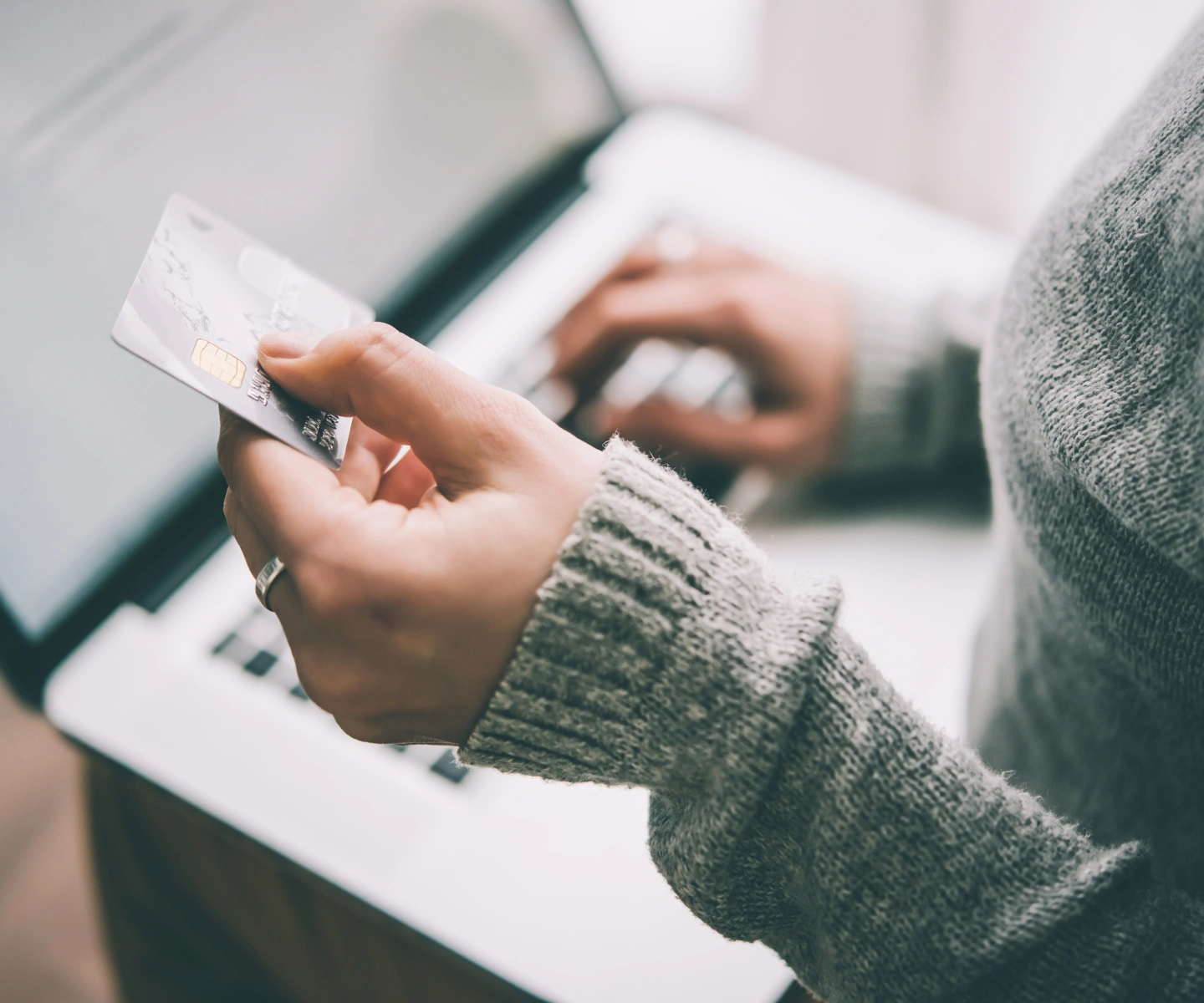 A closeup of someone holding a credit card while using their laptop to pay their Frontier bill