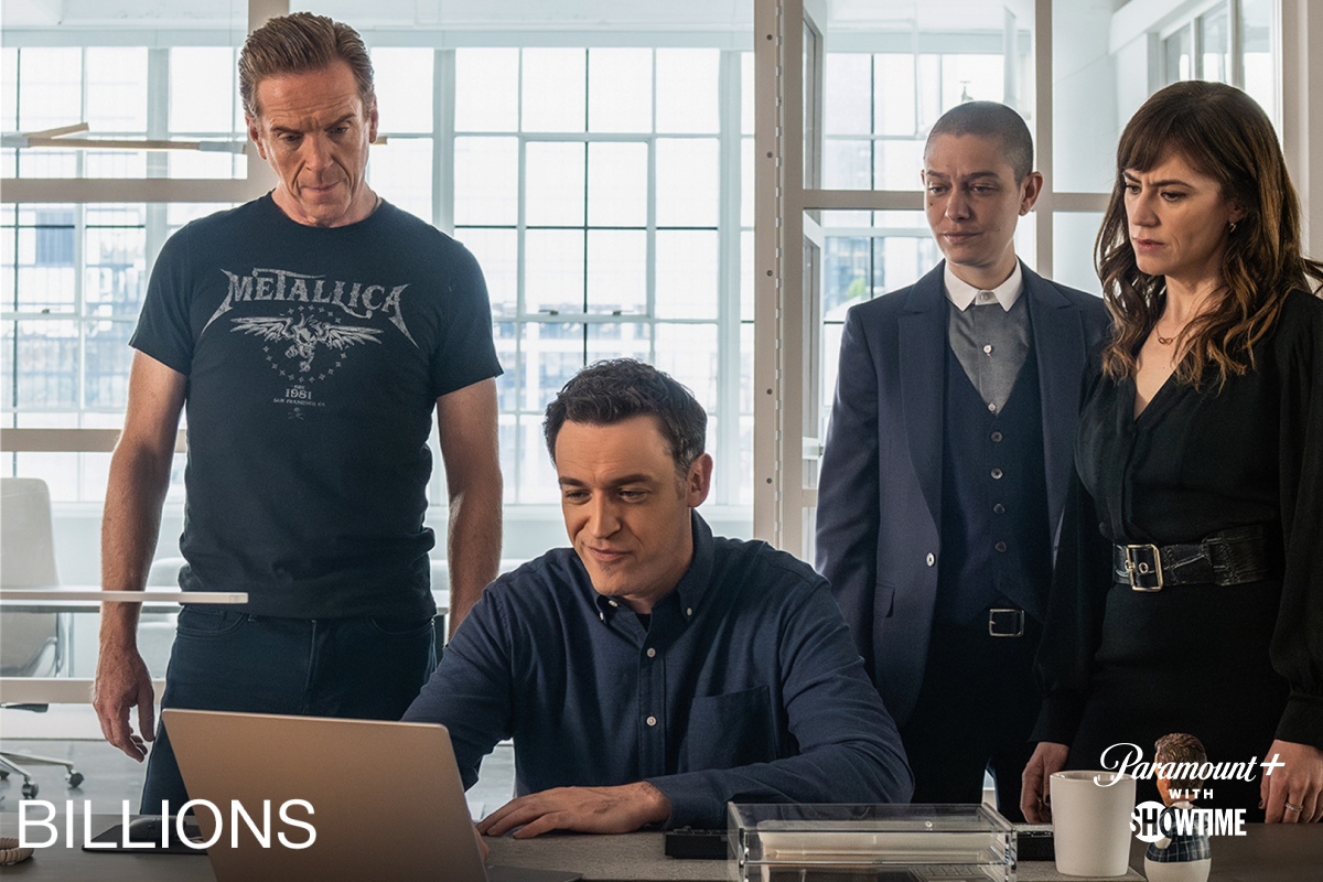 4 members on the Billions cast. One man is sitting with a laptop while the other three look over his shoulder.