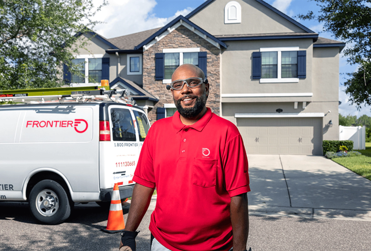 A male Frontier technician standing beside a Frontier work truck parked outside of a home