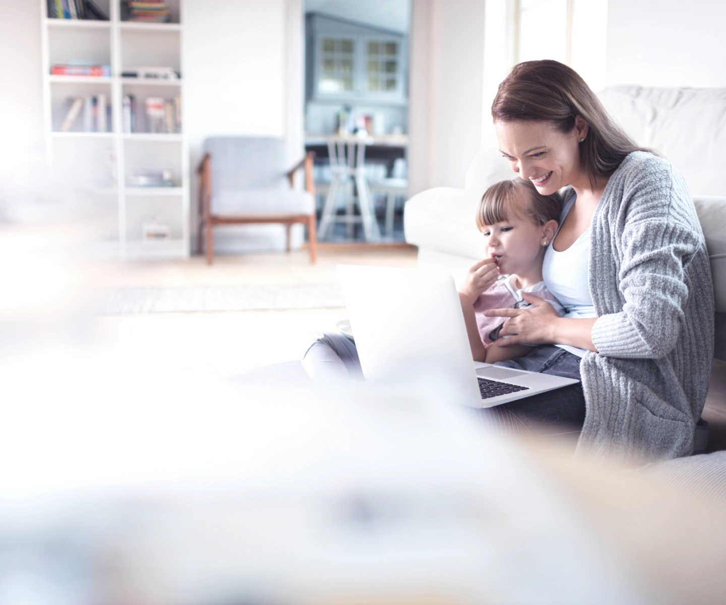 A woman leaning against the couch with her child while using Frontier internet on a laptop