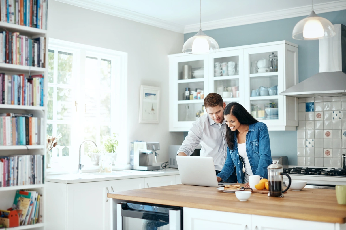 A couple in their well-lit kitchen looking at a laptop and using Frontier internet together.