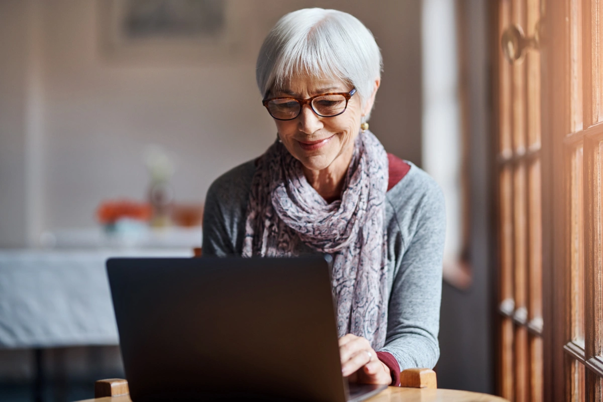 A mature woman in a gray scarf sitting at a laptop