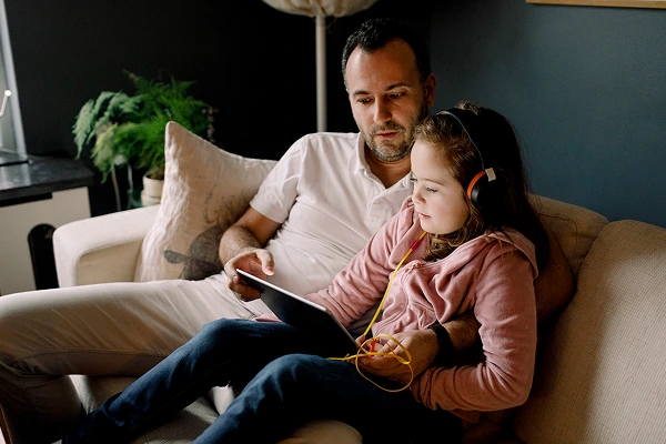 A smiling man and his daughter looking at a tablet together on a couch