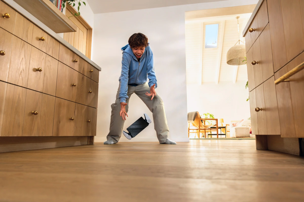 A teenager mid-reaction as he accidentally drops a handheld gaming device onto a kitchen floor