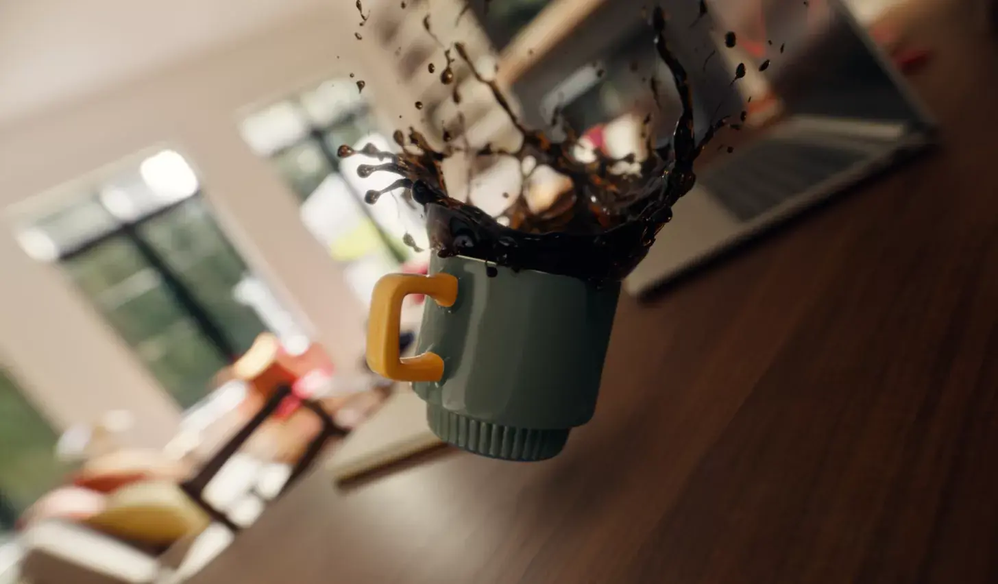 A coffee mug mid-air, spilling coffee across a desk toward a laptop.