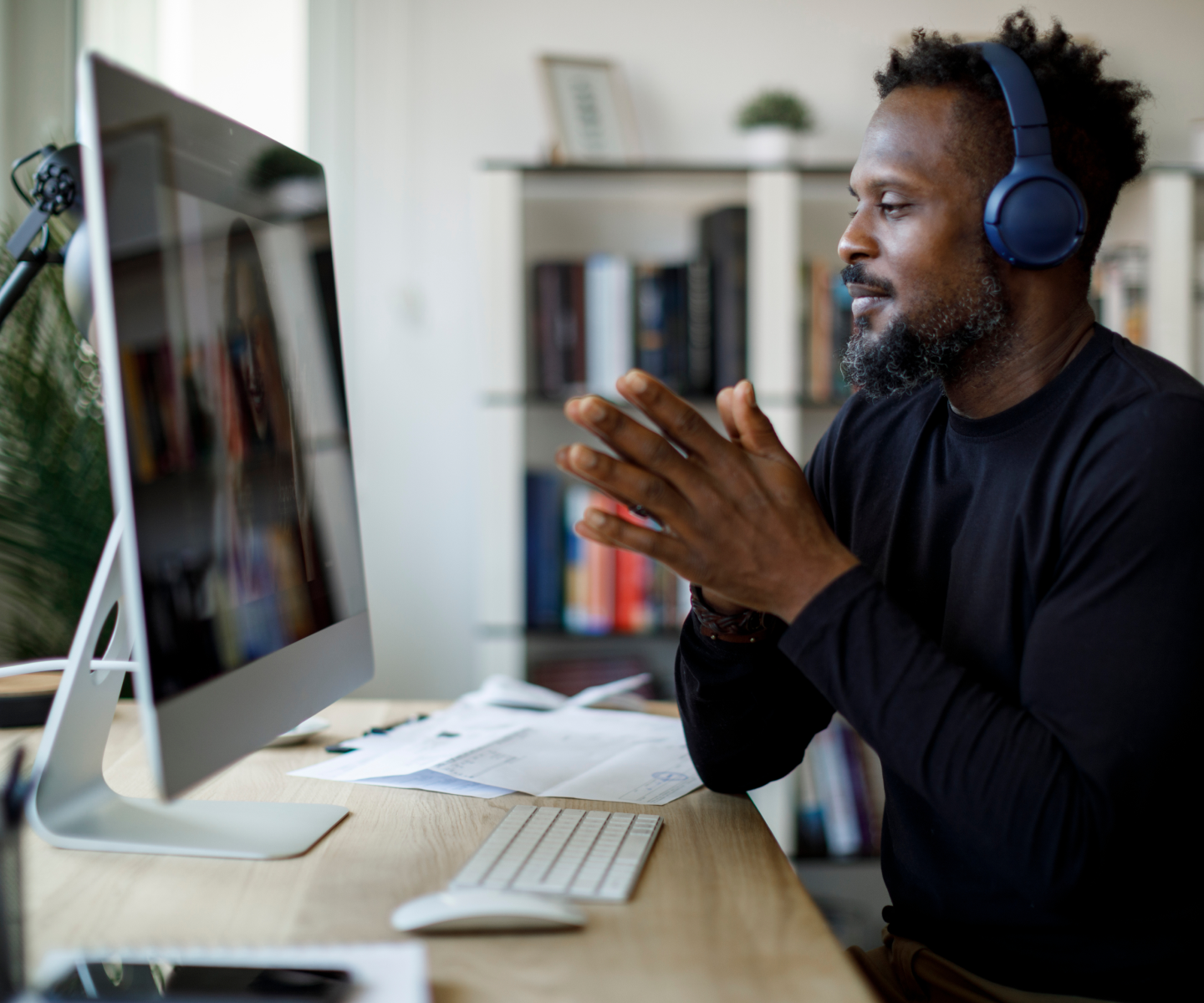 Man in black sweater and navy headphones video chatting on a desktop computer