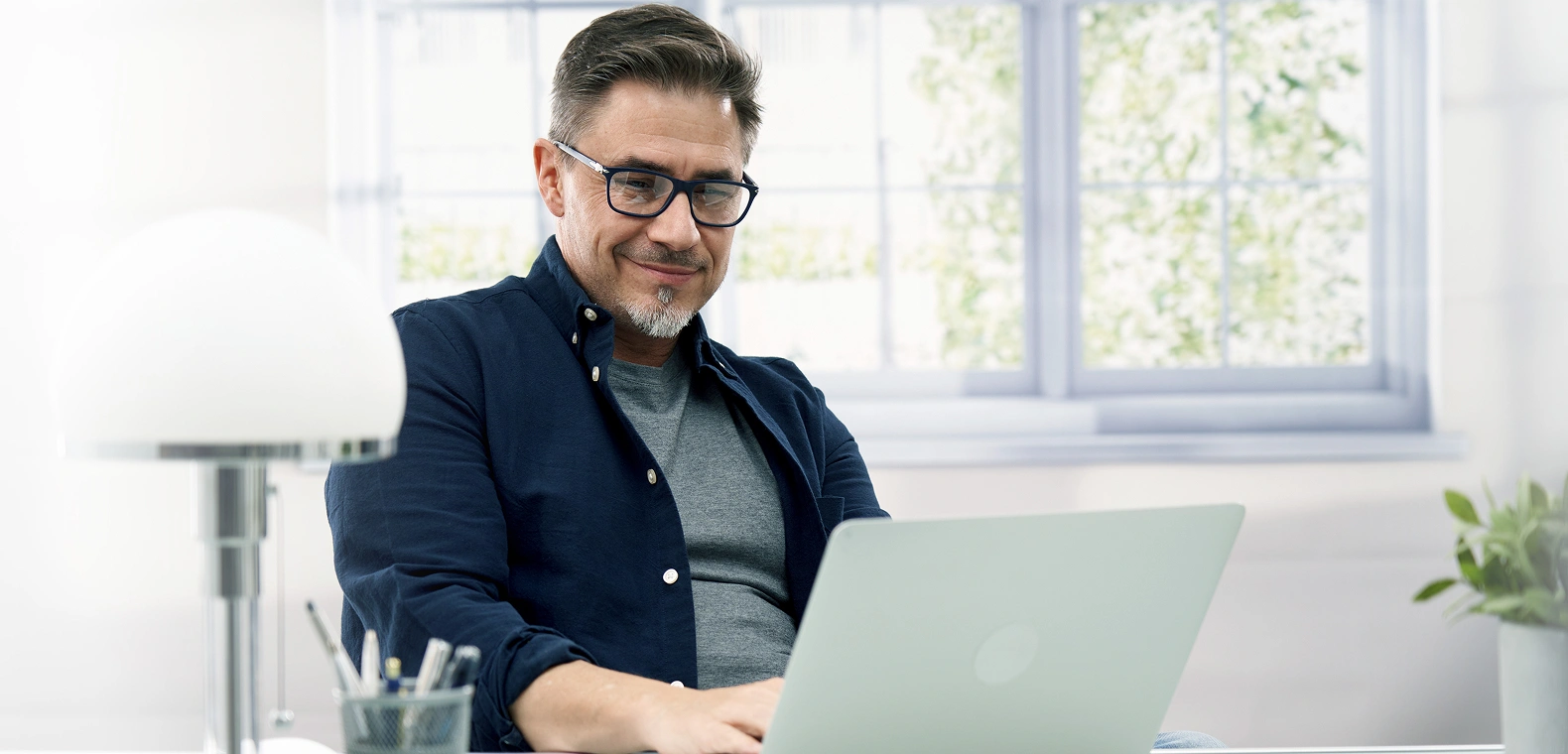 A man with glasses using a laptop in his home office to create a Frontier account online