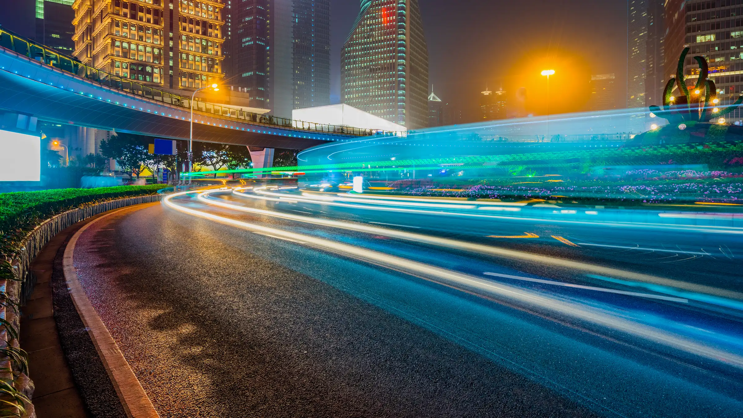 Image of a highway with lights with city skyscrapers in the background.