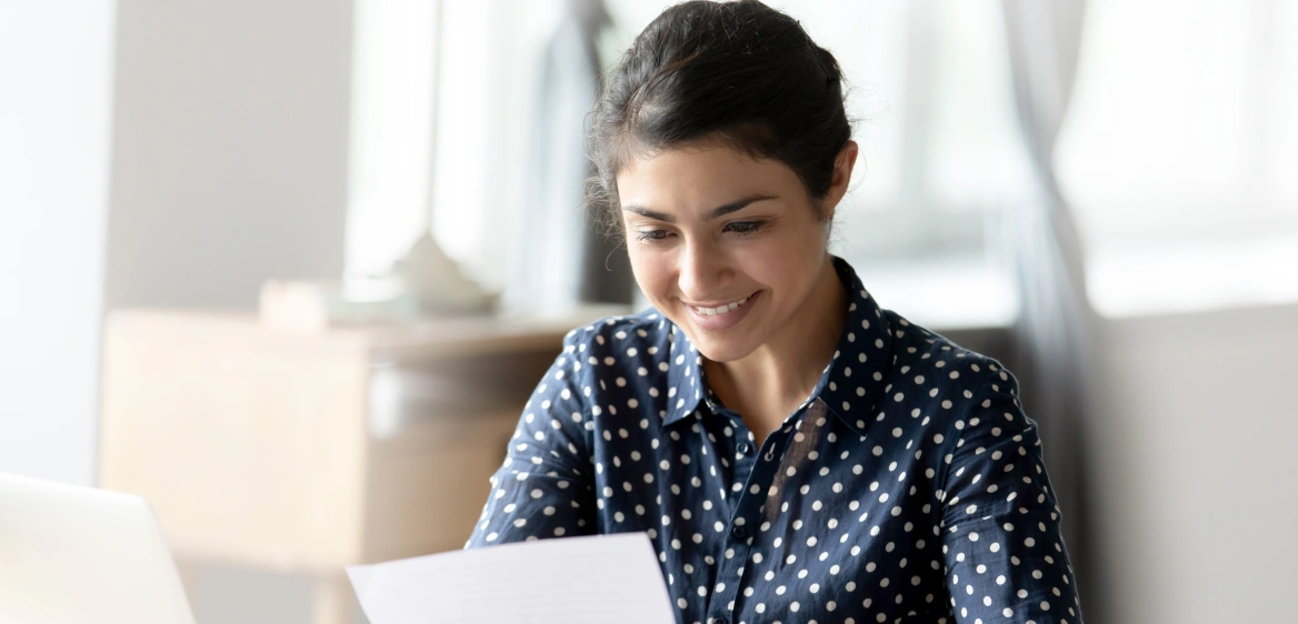 A woman sitting at her desk in front of a laptop and reviewing her paper bill