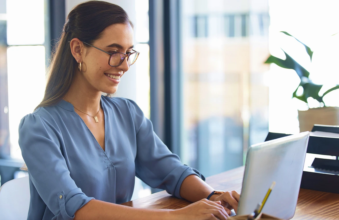 A woman working on a laptop at a desk in a bright modern office.