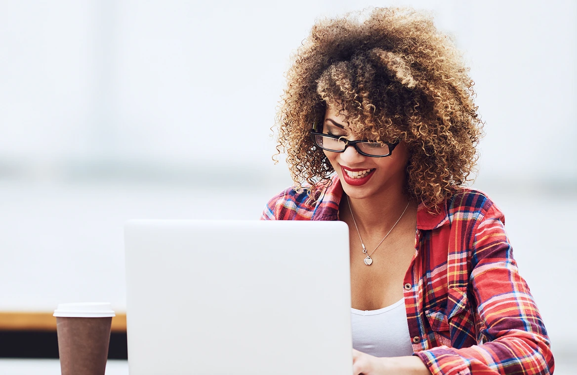 A smiling woman with curly hair looking down at her laptop