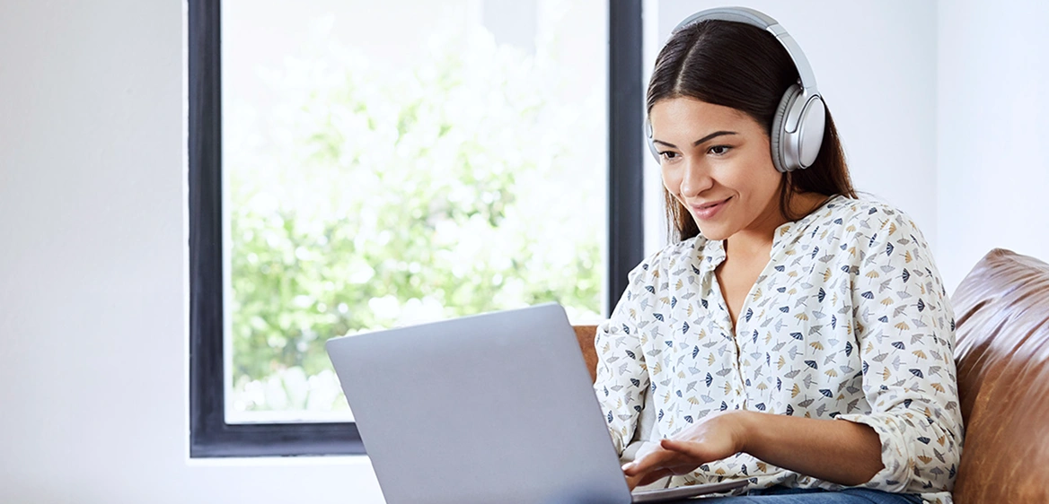 A woman wearing headphones and using her laptop while sitting on the couch