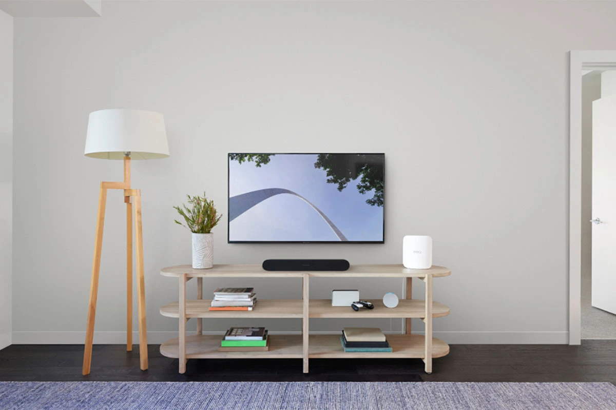 A modern living room with a wall-mounted TV, a black soundbar and a white eero mesh Wi-Fi router on a wood media console